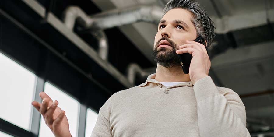 Salesperson sitting on edge of desk talking on his phone with one arm raised in conversation